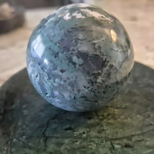 Polished blue-green stone orb on marble base
